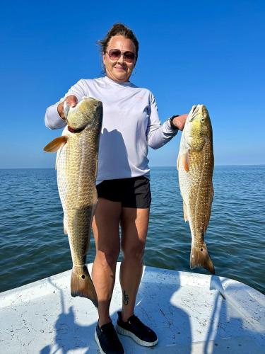 Angler holding two redfish on the bow of the boat
