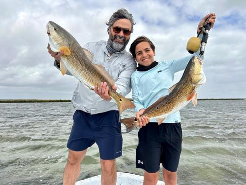 Father and son each holding a redfish